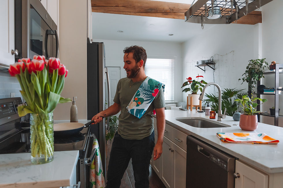 Man cooking in a bright modern kitchen with Hawaiian print kitchen towels on his shoulder and folded on the counter.
