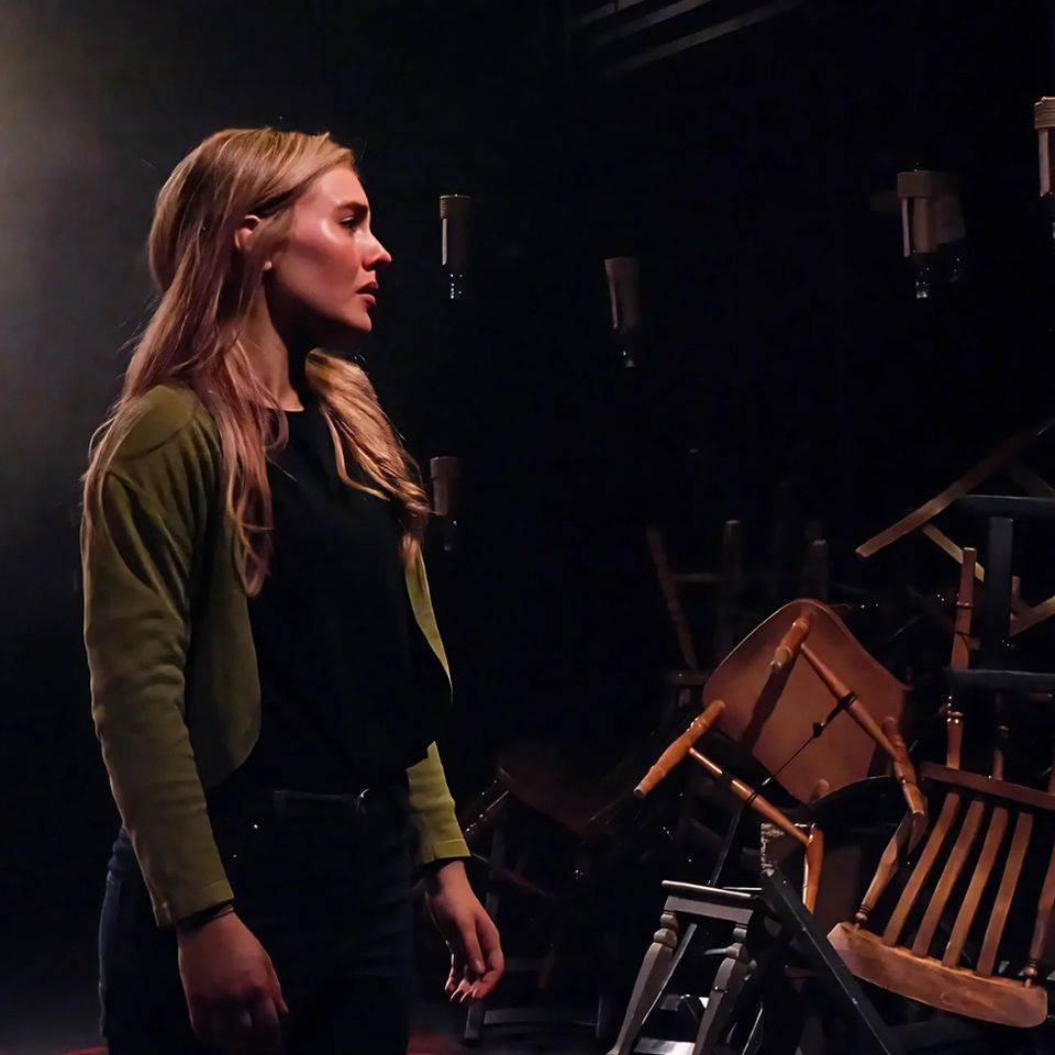 Actor in profile on dark stage, surrounded by equipment and dramatic lighting