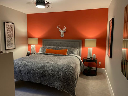 Cozy bedroom with orange accent wall, bed, lamps, and deer head decor Ferreras Design.