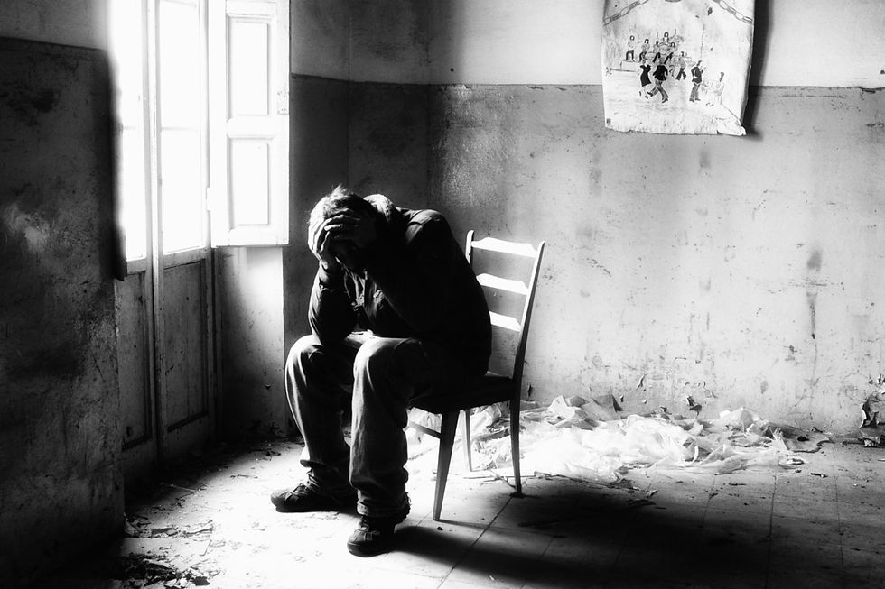 man sitting next to a window with his head in his hands