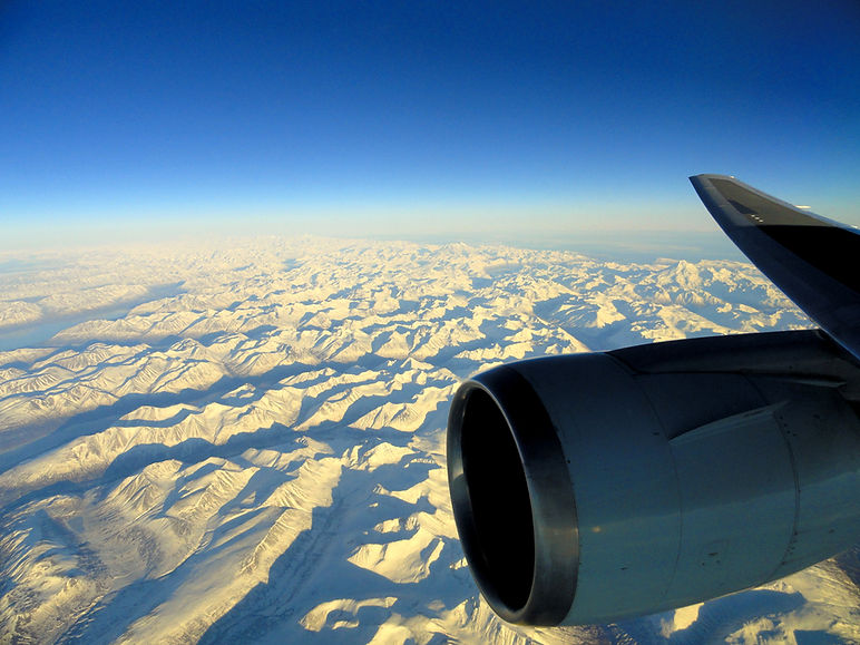Plane flying over Alaska mountains toward China at sunrise - representing cross-border journeys in our 2026 International Divorce Guide for expats and mixed couples
