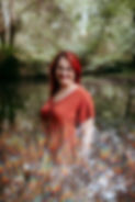 Photo de Roxane HERTZOG, une femme souriante devant une étendue d'eau, portant un haut brun rouge.