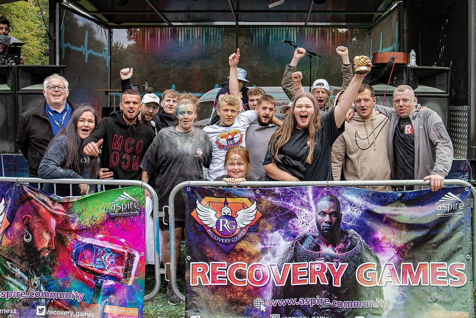 A group of people cheering behind a Recovery Games banner.