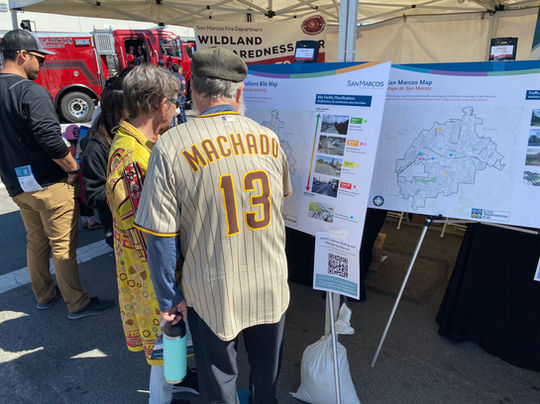 Two people stand in front of the interactive project map board, one wearing a Padres Machado jersey with a soft cap.