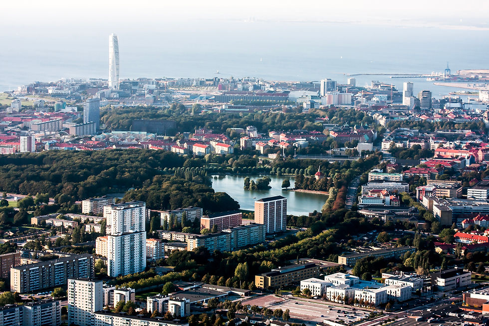 Flygvy över Malmö med Turning Torso i bakgrunden. Stadspark med sjö och skog syns. Stadsbilden domineras av höghus och tät bebyggelse.