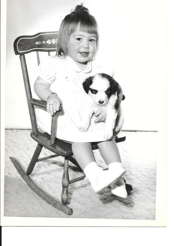 Toddler holding puppy in a rocking chair.