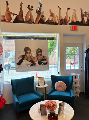 Interior photo of Harlow + James plus size boutique in West Des Moines, Iowa. Features elegant teal velvet chairs, empowering body-positive artwork showing diverse legs, bright natural lighting, and welcoming atmosphere. Perfect for showcasing the comfortable, inclusive shopping experience at Iowa's premier curvy fashion destination.