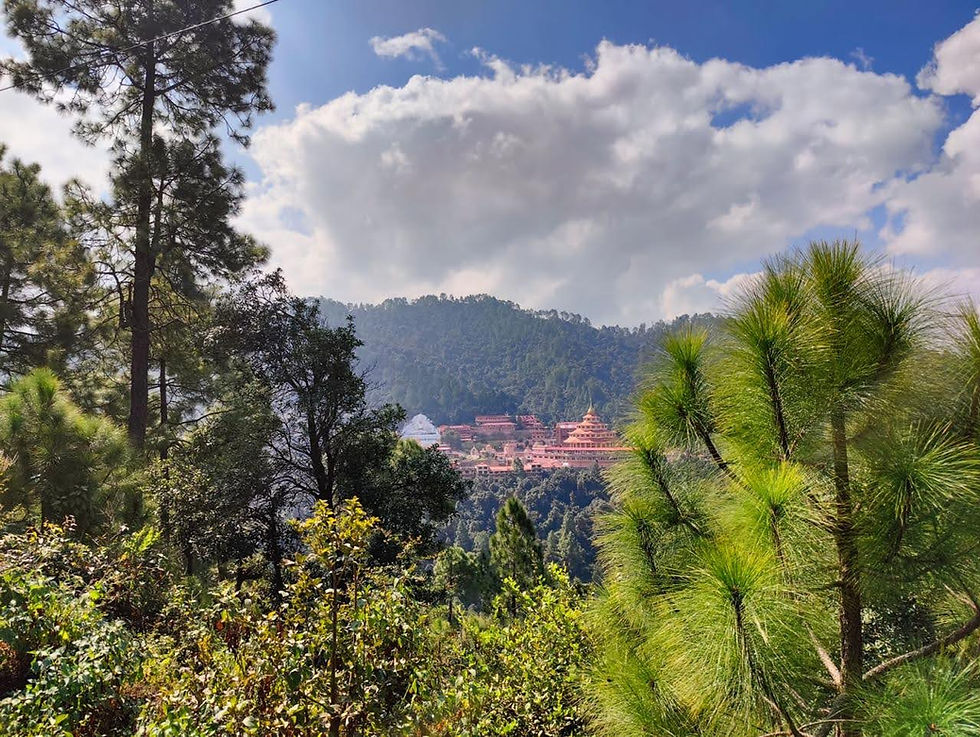 Lush green forest with a distant monastery in red and gold under a blue sky with clouds, conveying a serene and peaceful atmosphere in Kumaon region.