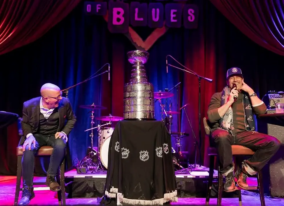 Two people on stage (Darren Pang and Jon Hamm) with the Stanley Cup between them at a Spark Bookings & Creations event.