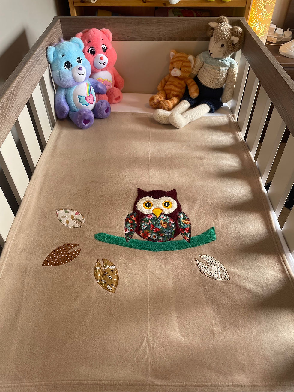 Thumbnail: Handmade beige fleece blanket with owl design layered in crib, made in Ireland by The Owl Tree