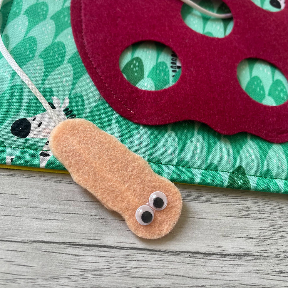 close up of worm used to thread cord through felt apple in toddlers busy book page