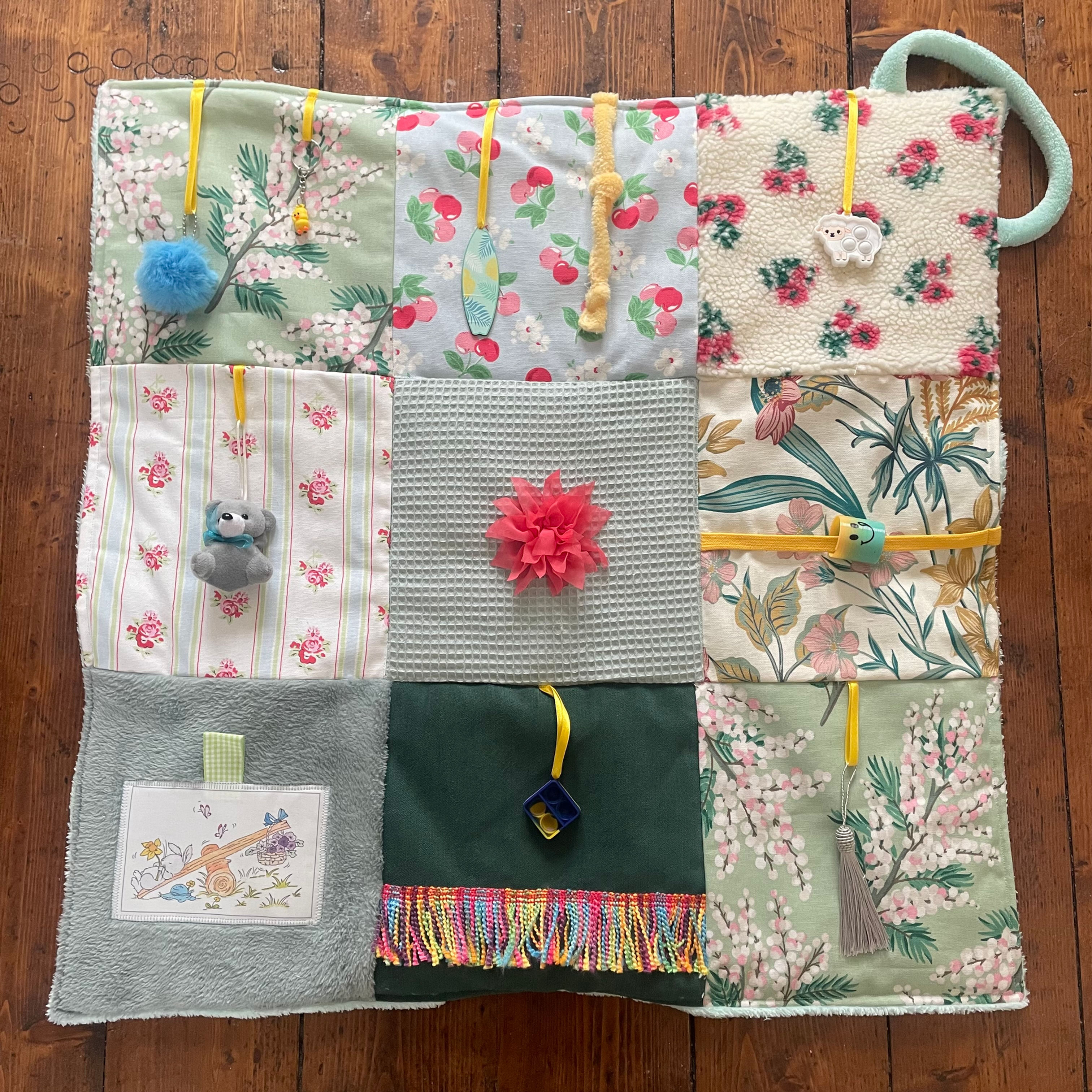 Patchwork dementia fidget blanket with sensory attachments and rope handle.