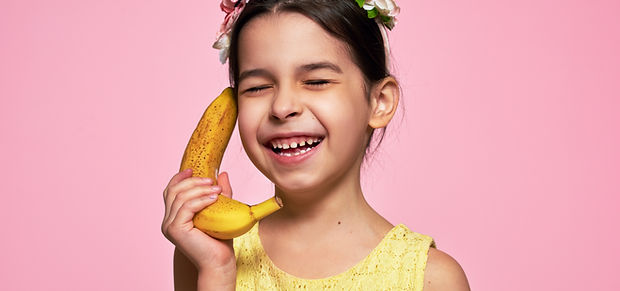 A candid portrait of a joyful smiling little girl holds a banana, like a phone, isolated o