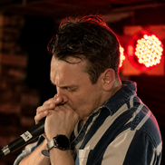 Local musician from 'The Back River Rats' playing the harmonica into a microphone on stage