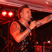 Robbie Williams Tribute act performing on stage holding a microphone and water.