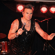 Robbie Williams tribute act singing into a microphone on a stage with red lights