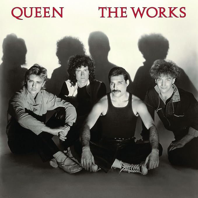 Album cover art for Queen's the works, displaying a black and white portrait of the band members, sat on the floor