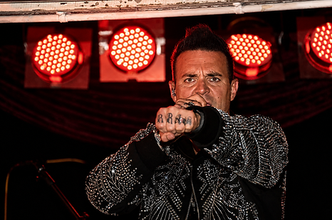 Robbie Williams tribute act, live in stage, striking a classic 'Robbie' pose with arm extended and fist clenched.