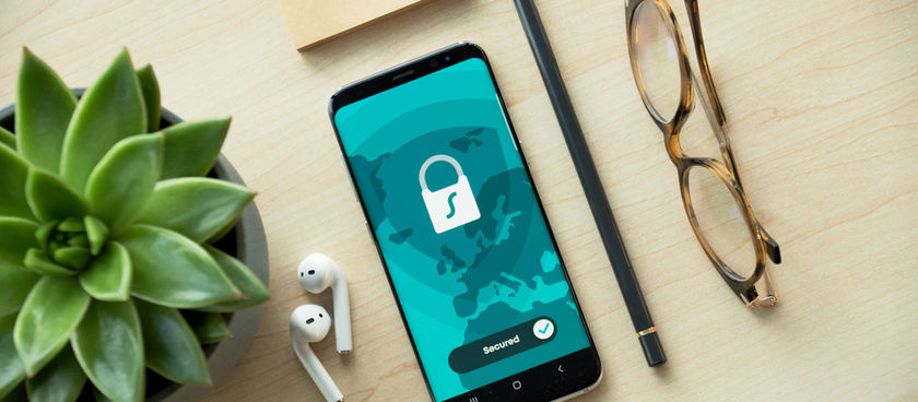 A picture of a phone with a lock screen on a desk with earpods, a pencil, glasses, and a plant.