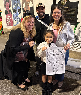 Live caricature artist Kathy Buskett poses with a happy family displaying their finished caricature at LoDa ArtWalk in Mobile, Alabama.