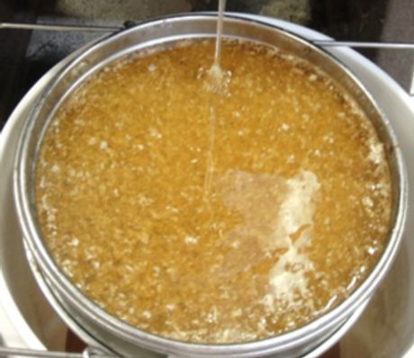 Raw honey being filtered through a stainless steel sieve.