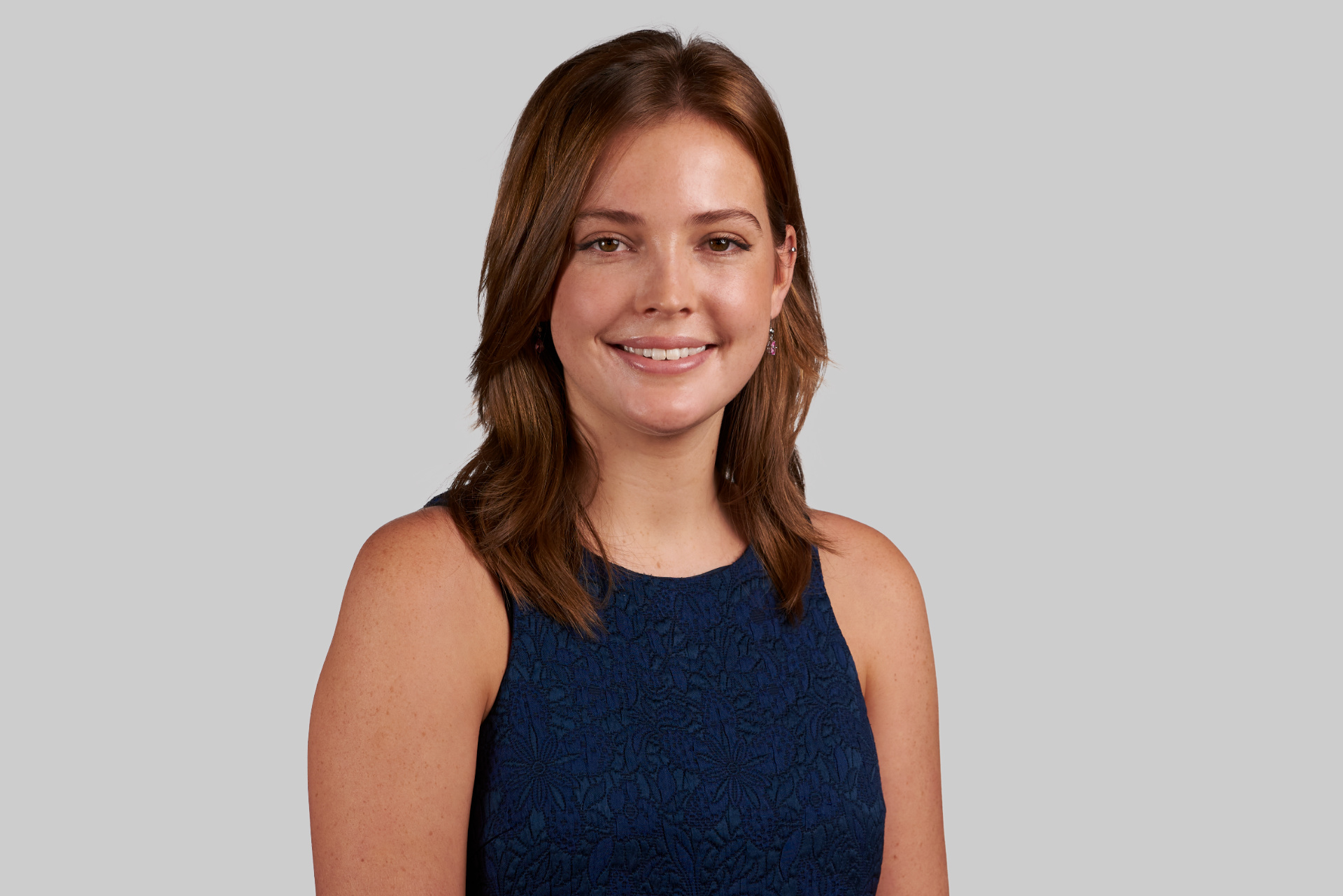 Smiling young woman with brown hair wearing a dark blue top.