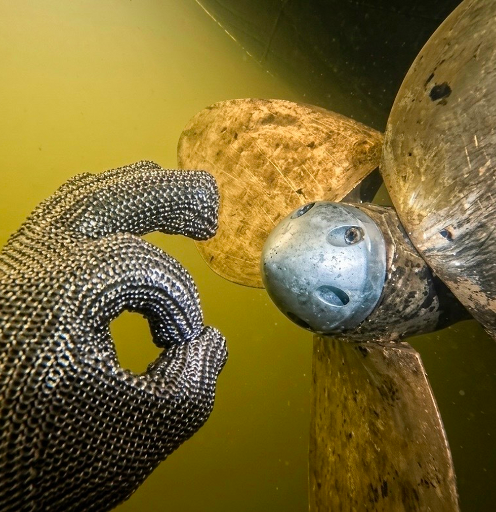 Hand in chainmail glove makes 'OK' sign by propeller underwater