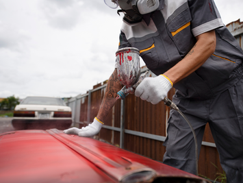 Worker in respirator painting red car part