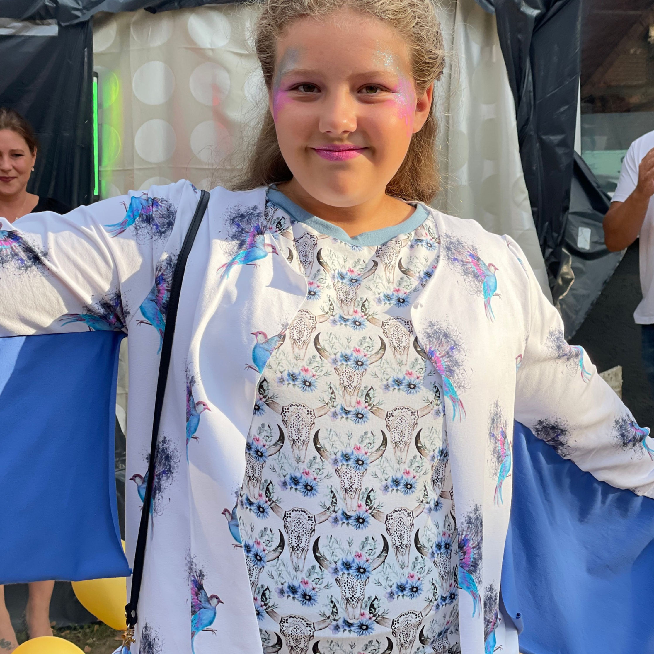 Mädchen mit selbst genähter Kleidung auf Laufsteg, lächelt, breitet Arme aus, hat Flügelärmel