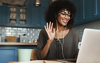 Image of person receiving 1:1 coaching, waving at the camera and wearing ear buds while smiling and looking at a laptop