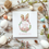 Thumbnail: white square card with an easter themed wreath with easter eggs and bunny ears. pink theme