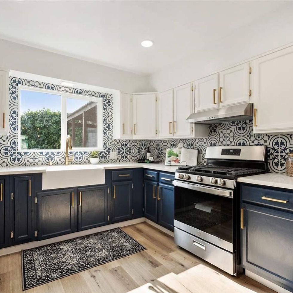 A bright kitchen featuring navy lower cabinets, white upper cabinets with gold hardware, a patterned blue and white tile back