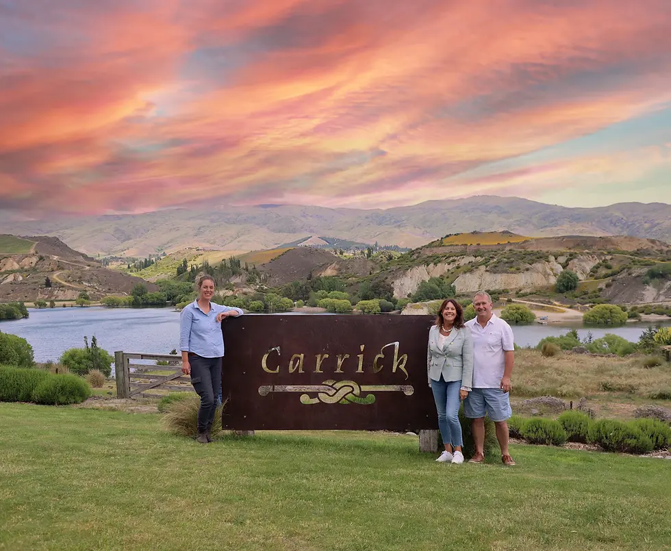 Alison and Tony Cleland, owners of Carrick, pose with chief winemaker Rosie Menzies, set against a stunning sunset backdrop overlooking their picturesque vineyard.