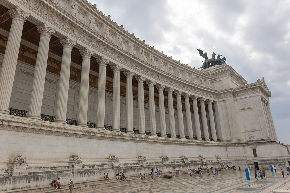 Monument to Victor Emmanuel II, Alter of the Fatherland, with tall columns and a chariot sculpture on top. People sit and walk in the foreground against a cloudy sky.