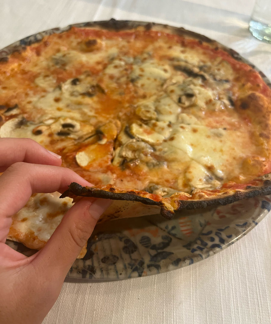 Close-up of a Margherita pizza in the Jewish Ghetto of Rome, with a hand lifting a slice to reveal its thin, crispy crust and melted cheese topping.