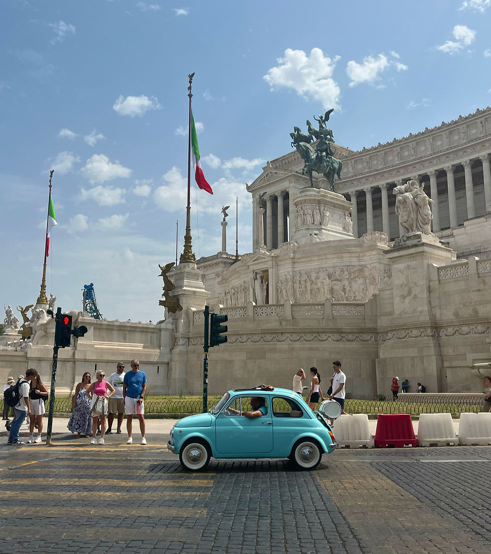 Small blue Fiat driving past the Altare della Patria in Rome.