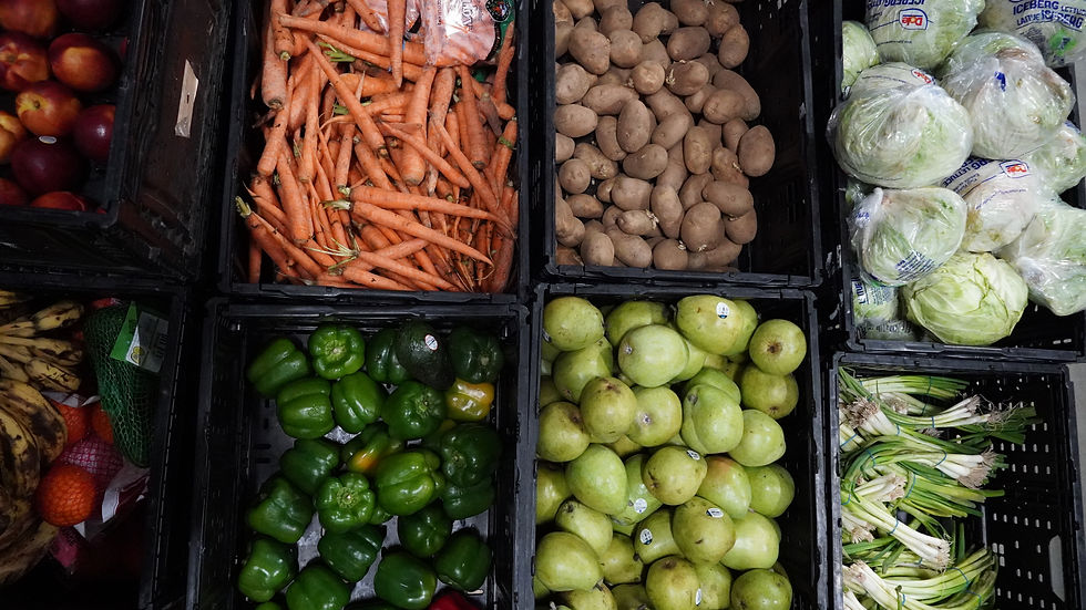Crates of fresh produce including carrots, potatoes, lettuce, bell peppers, pears, bananas, and green onions arranged in a market display.