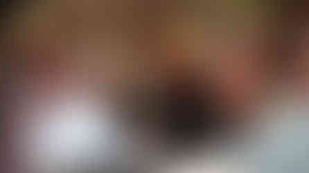 In a crowded room, a woman sits and laughs as two gentleman tell stories.