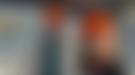 A man and a woman wearing orange construction hats smile while taking a selfie in a construction zone.