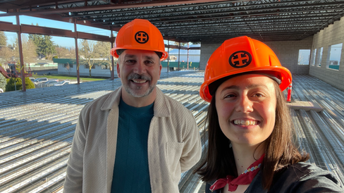 A man and a woman wearing orange construction hats smile while taking a selfie in a construction zone.