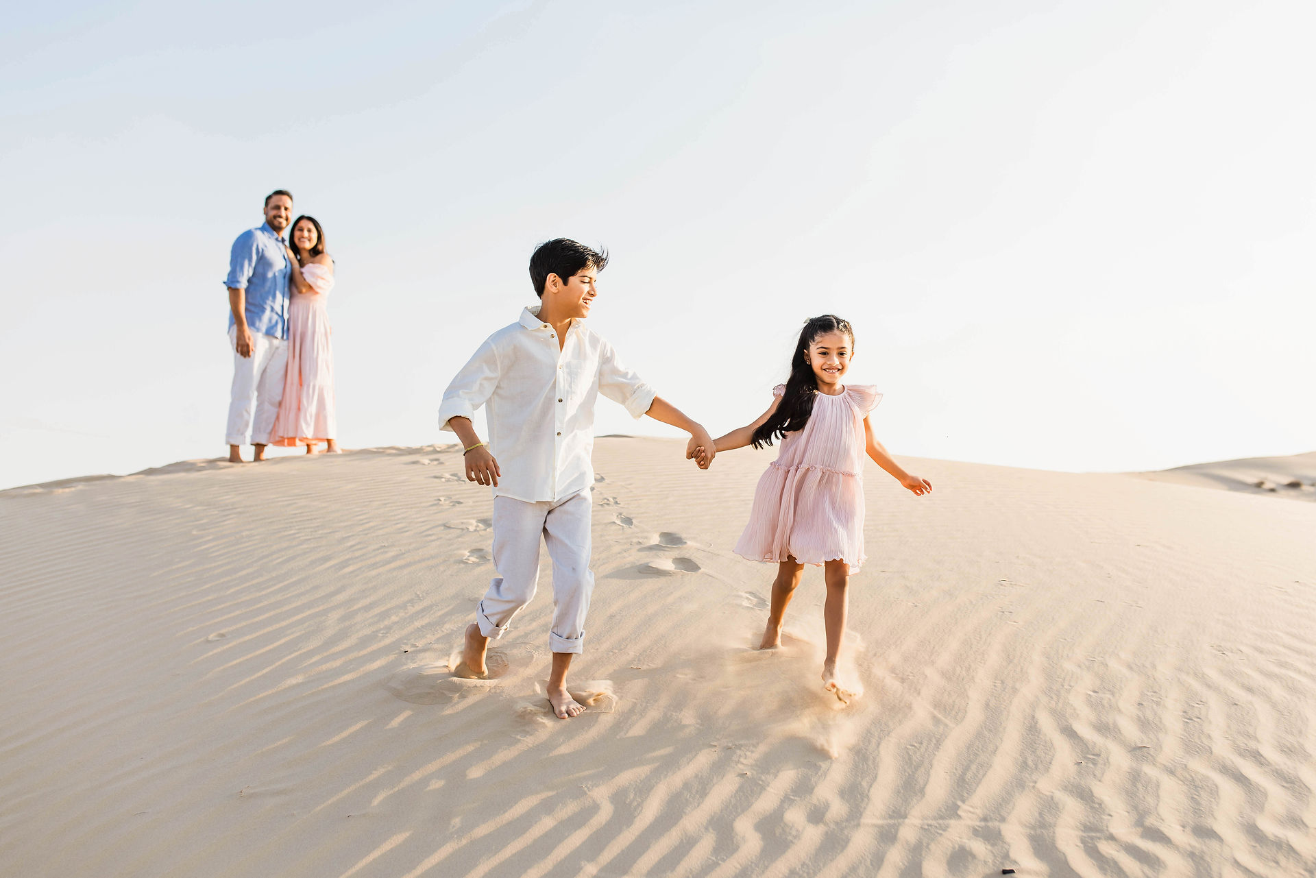 Siblings running down the dune Abu Dhabi desert photo shoot