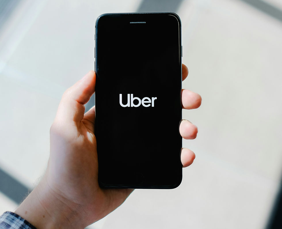 30 x 100,00 Avios to be Won With Every Uber Journey You Take. Hand holding a smartphone displaying the Uber logo on a black screen. Background is softly lit and neutral-toned, creating a calm mood.