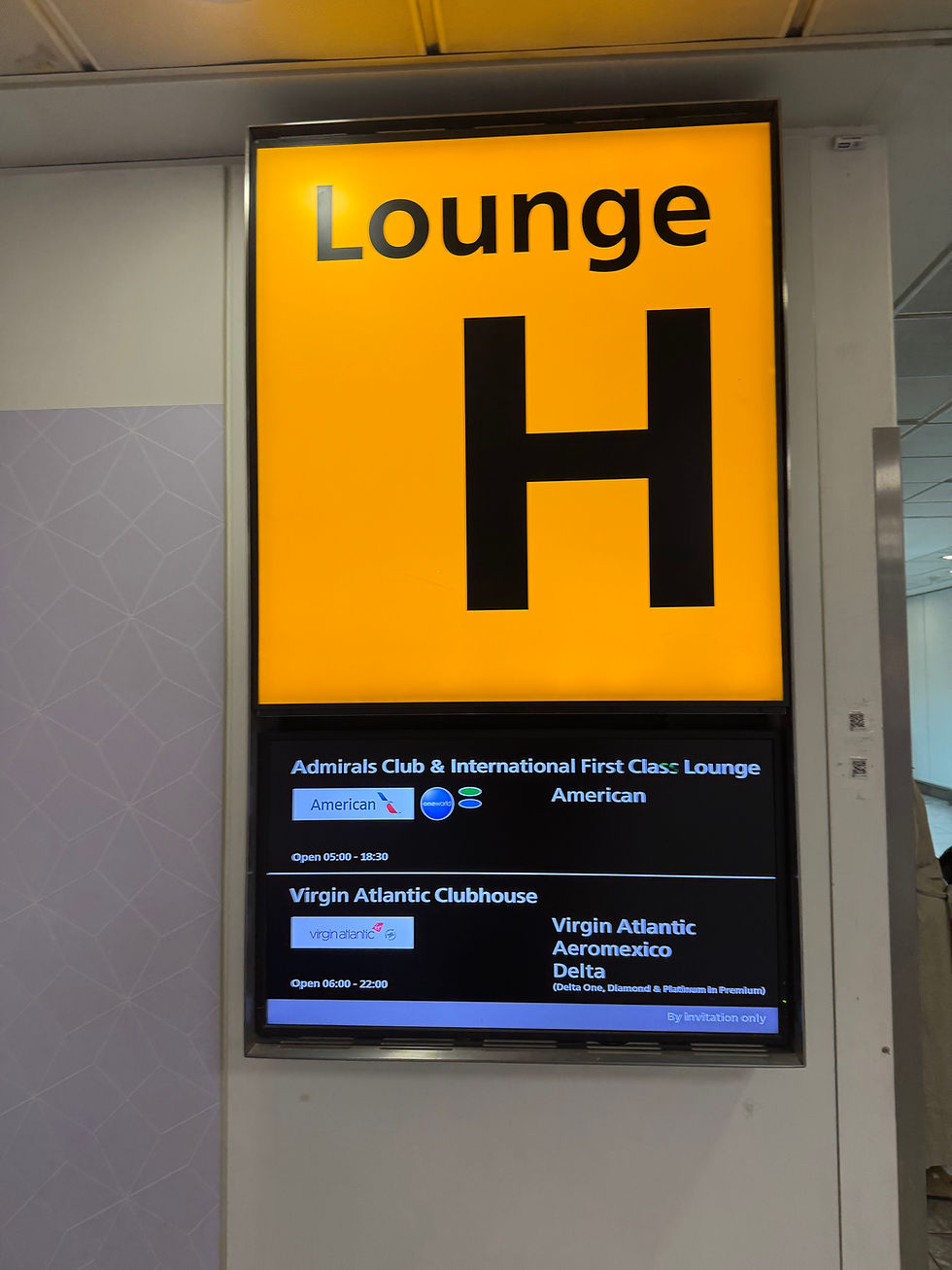Yellow sign with "Lounge H" above a black display listing lounge names and hours, including Admirals Club and Virgin Atlantic Clubhouse.