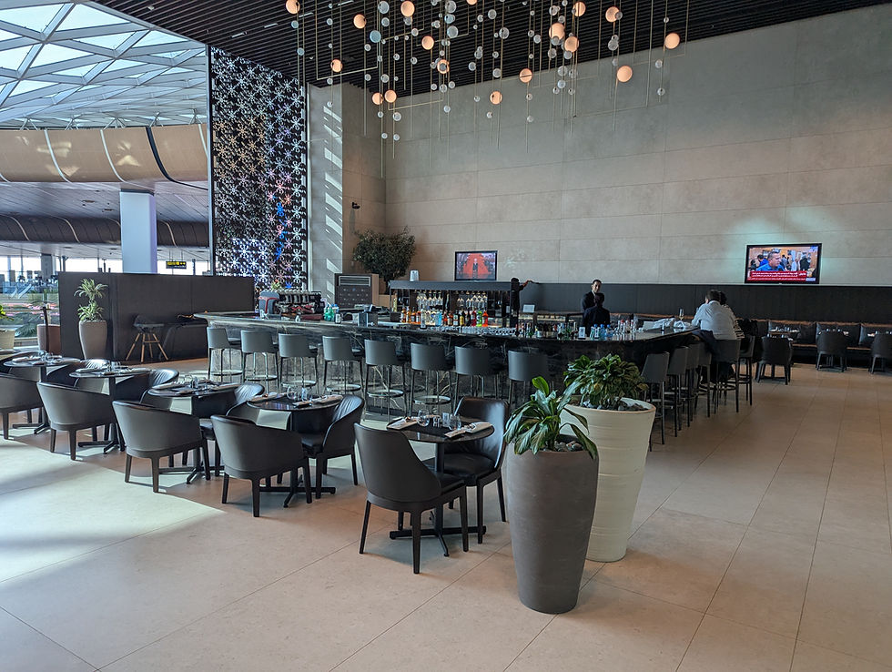 Al Mourjan Garden Lounge bar.. People sit at the bar, with plants nearby and TVs on the wall, creating a relaxed atmosphere.