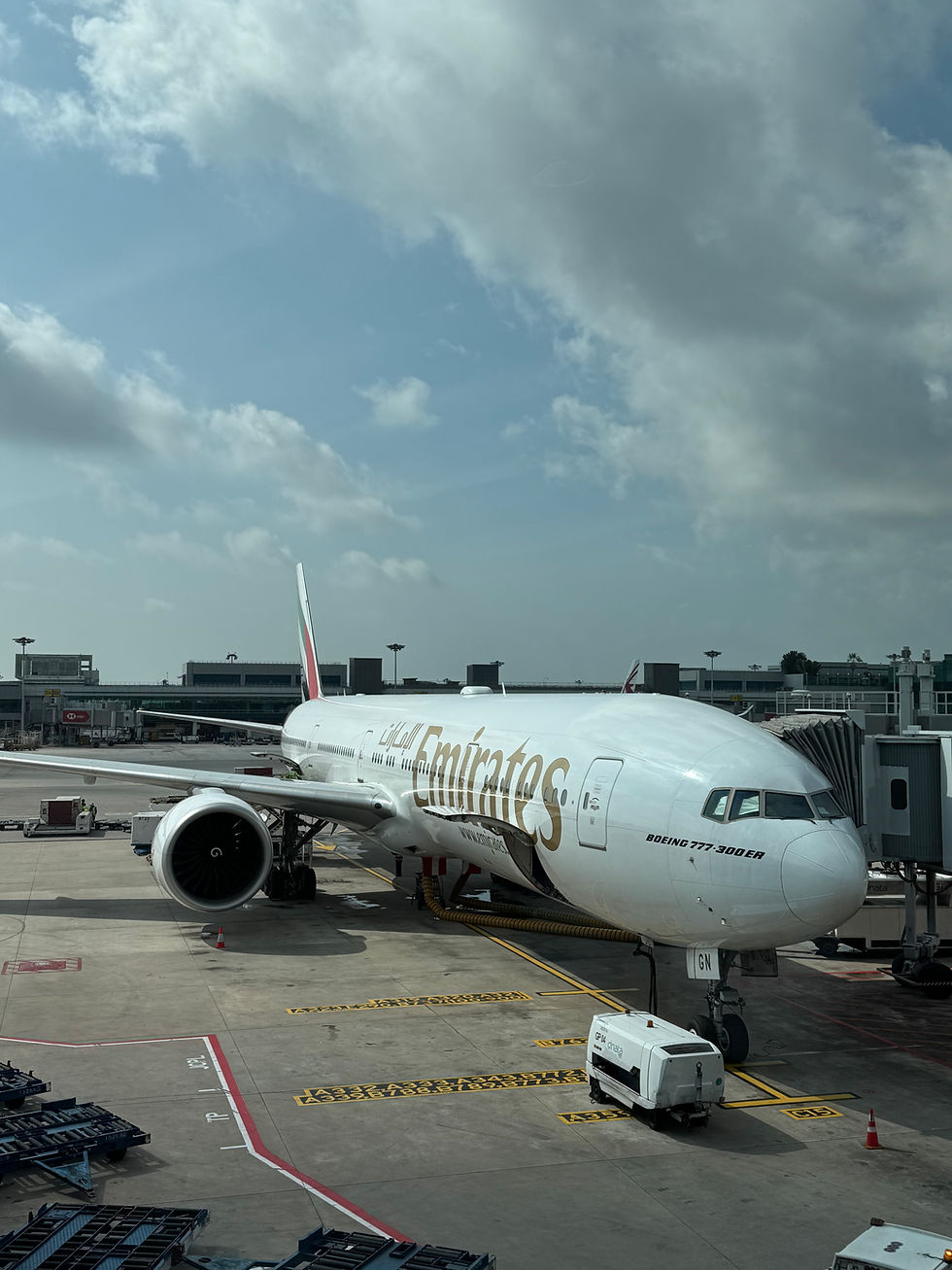 Emirates plane parked at airport gate under cloudy sky. Ground equipment nearby, with visible "Emirates" logo and "Boeing 777-300ER" text.