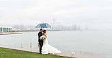Bride and groom under an umbrella at Lake Michigan with Chicago skyline behind them