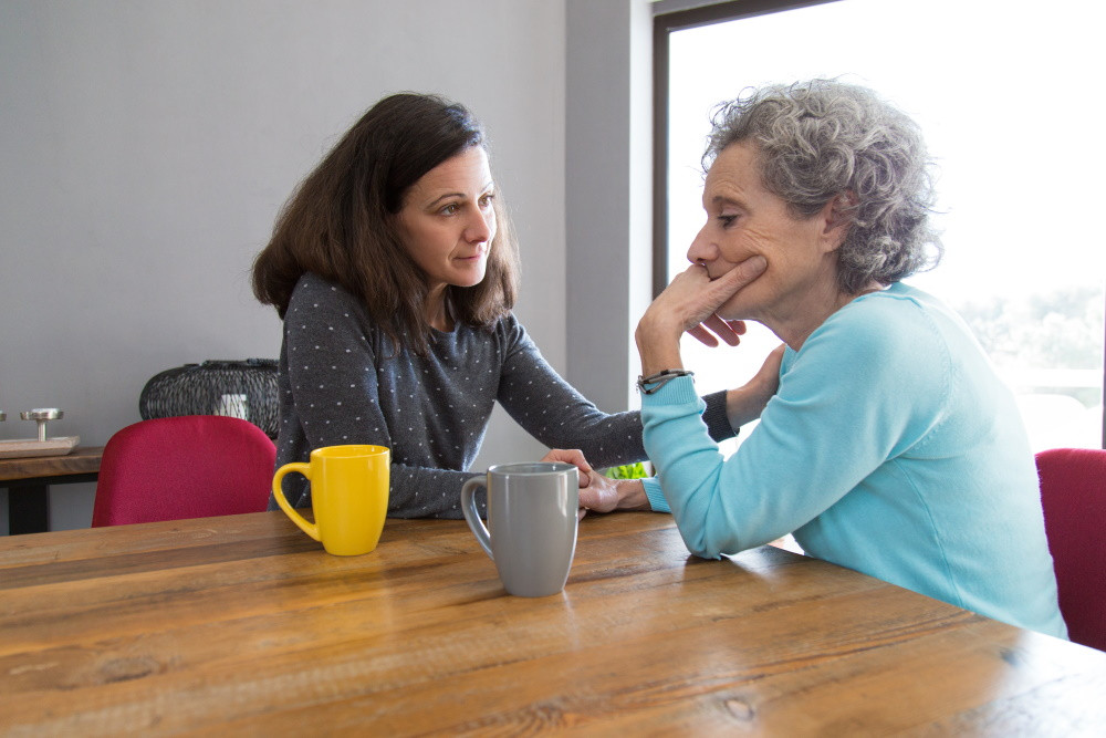 senior woman with anxiety sitting at a table with her daughter