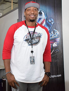Tyrone Dennis, Founder & CEO of Clippers & Cops in front of the Clippers and Cops original logo banner