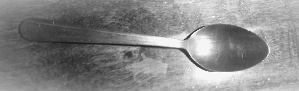A single metal spoon lying flat on a worn, textured surface, photographed in black and white. Symbolizes the last spoon in spoon theory.