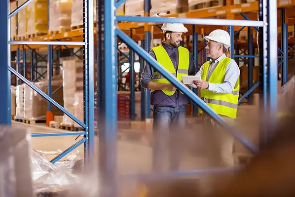 Zwei Fachberater in Warnwesten diskutieren im Lager diskutieren Lagererweiter-Regalerweiterung. mk-Lagertechnik.